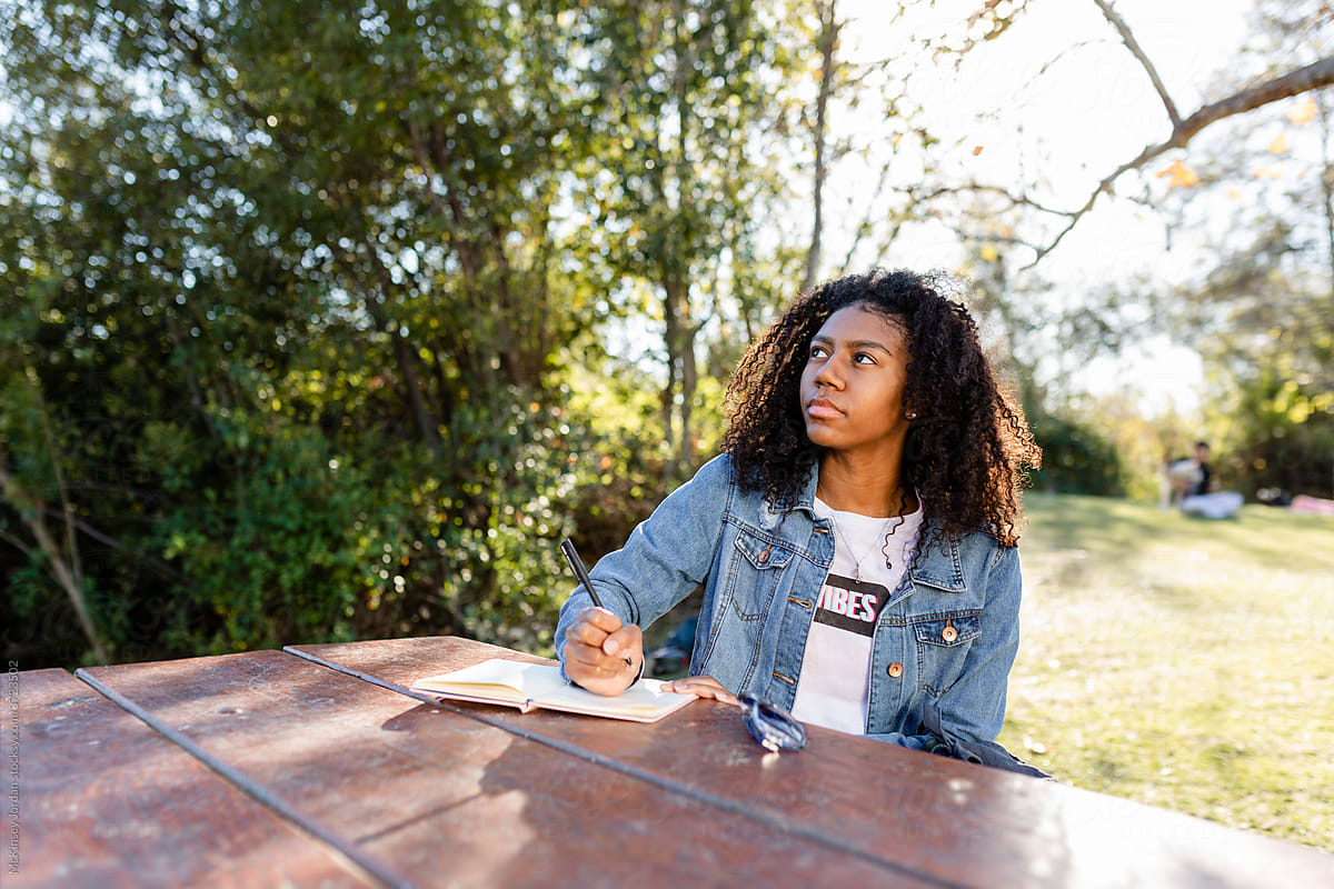 Young Woman Thinks While Writing in Her Notebook at the Park