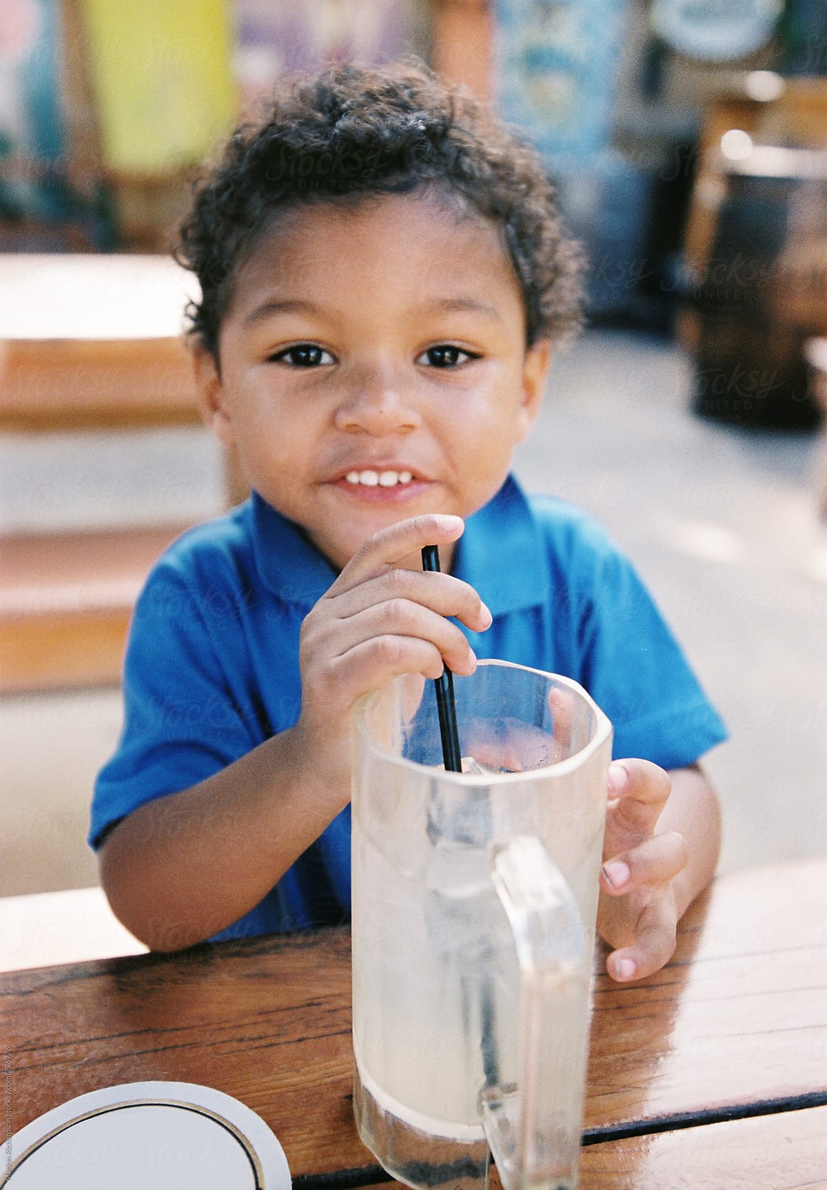 Mixed race child sitting, looking, and drinking from a tall glass.