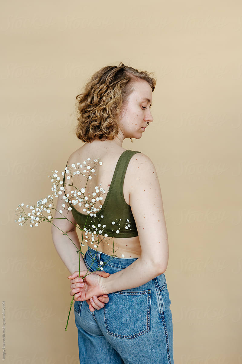Young woman with fragile flowers behind back