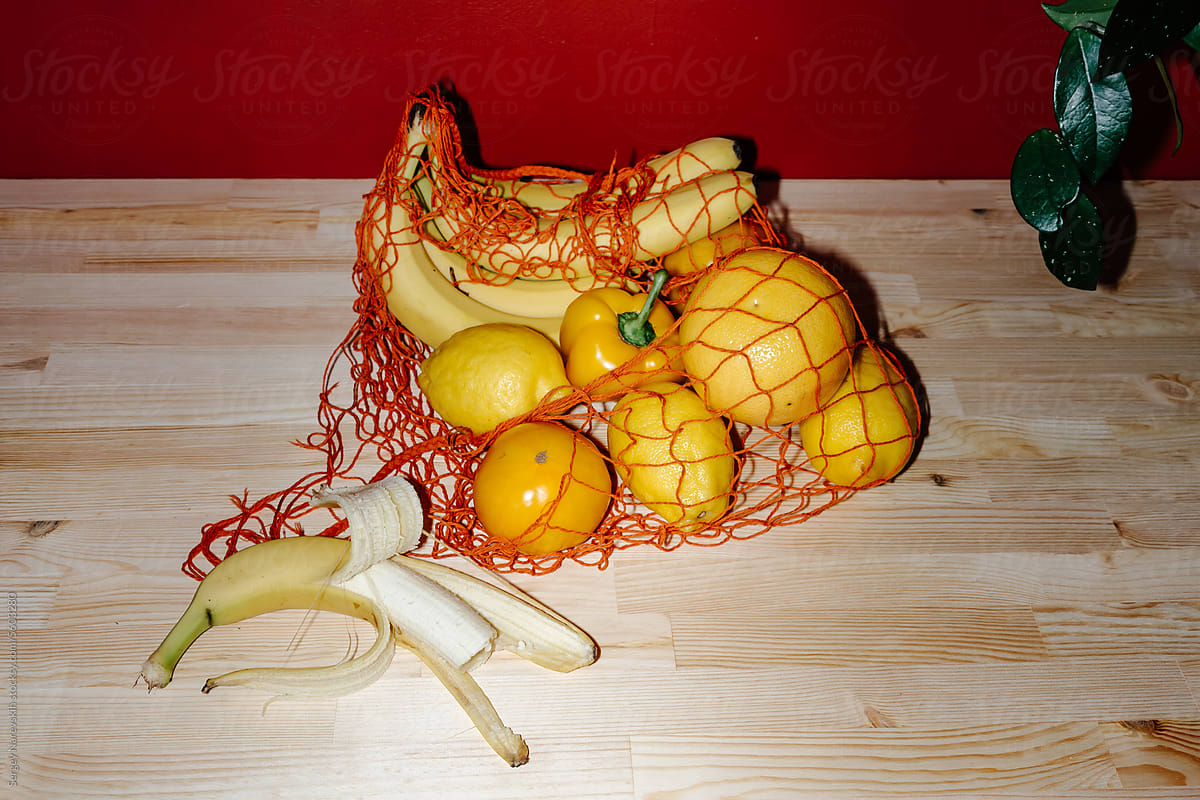 Orange mesh bag with yellow groceries and bitten banana