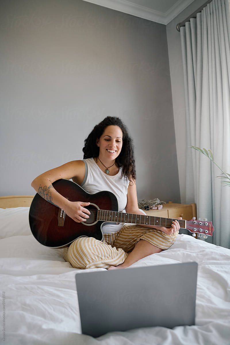Happy young woman learning guitar online with laptop