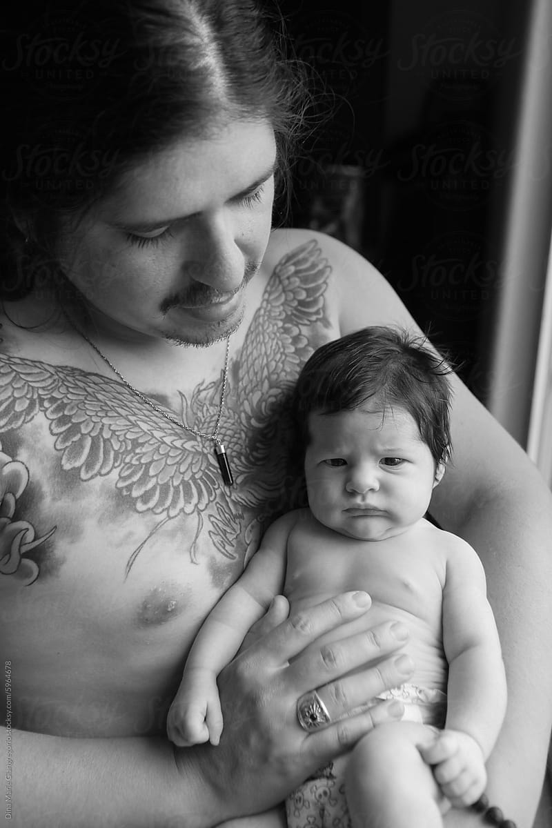 Tattooed Dad Holding Dark Haired Baby Up Against His Chest.