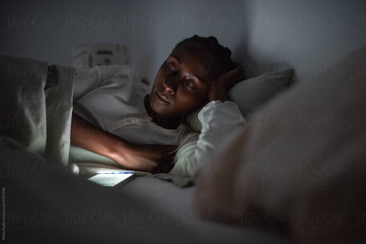 Black woman falling asleep in bed with smartphone