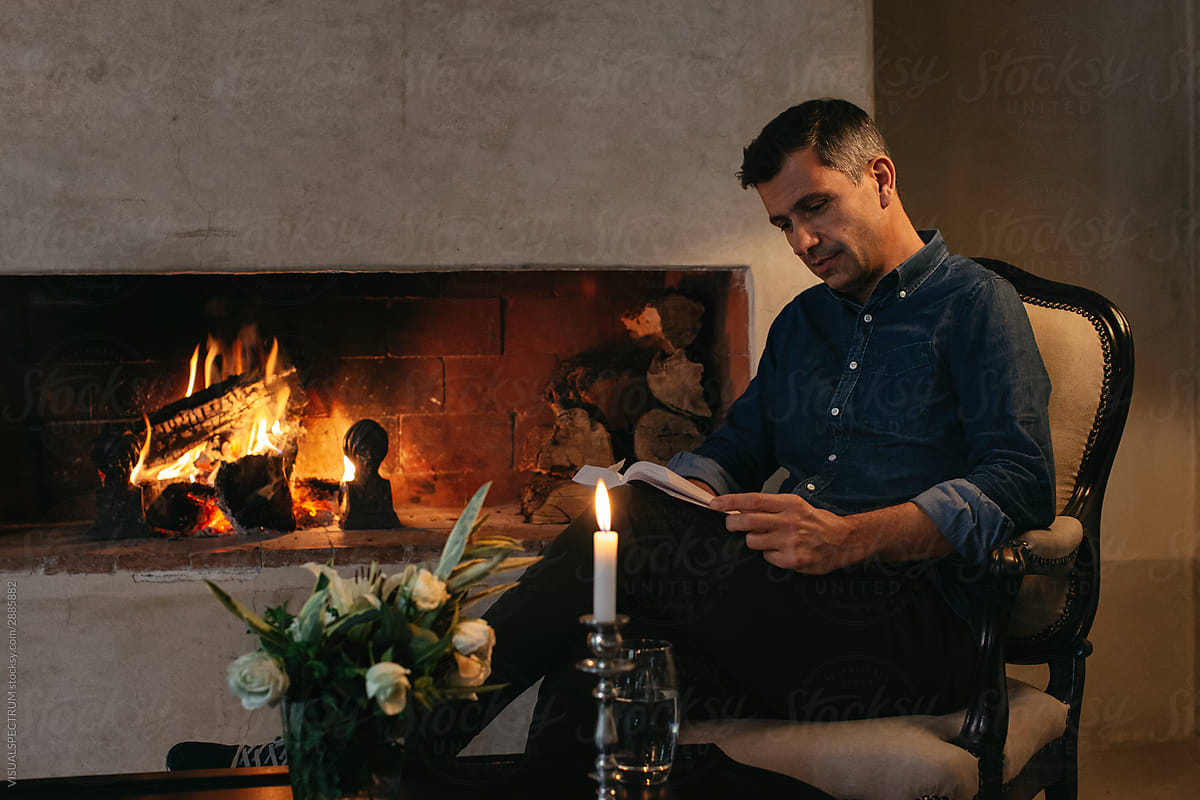 Handsome Caucasian Man Reading Book by Fireplace