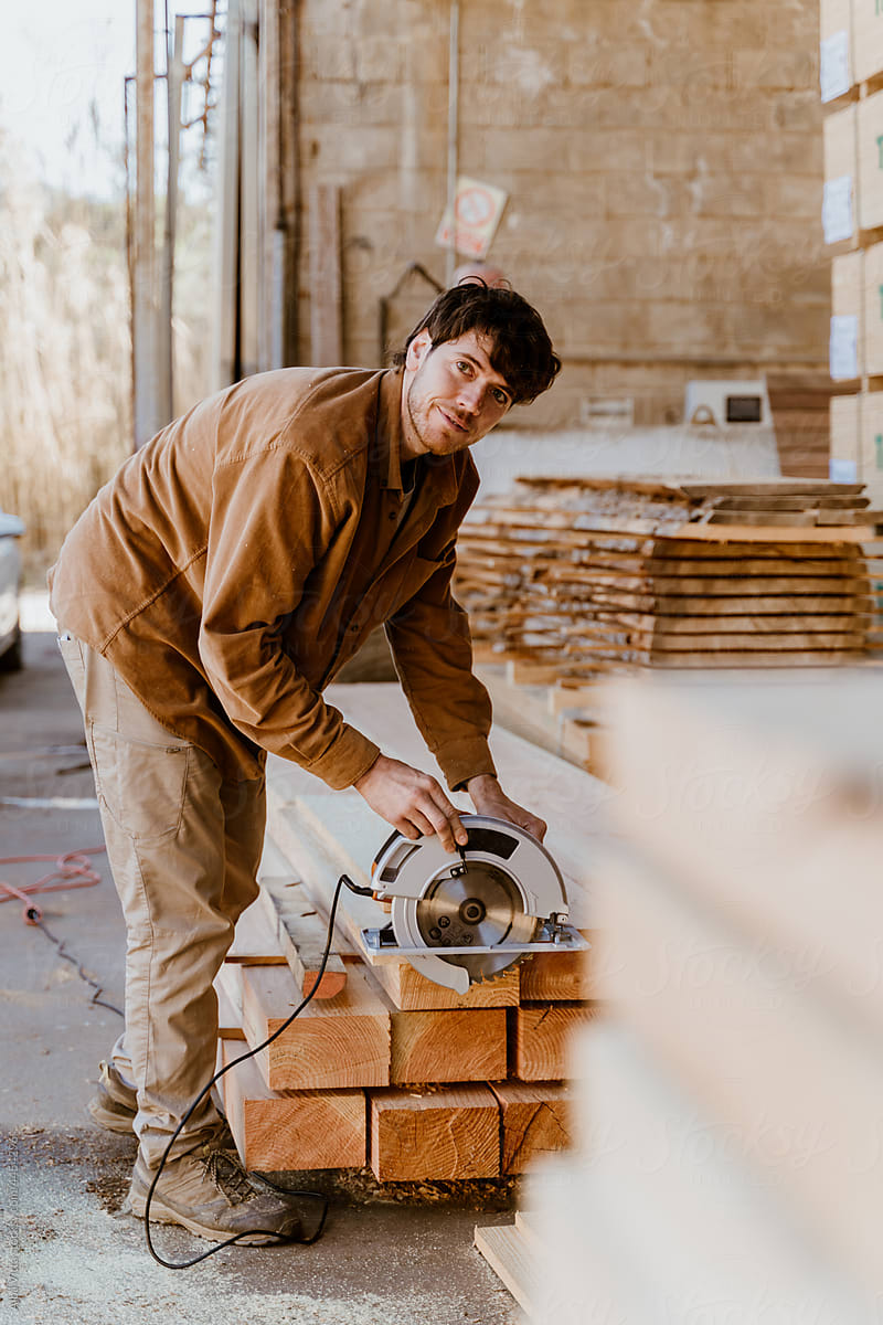 Portrait of man sawing Wooden boards at lumber mill looking at camera
