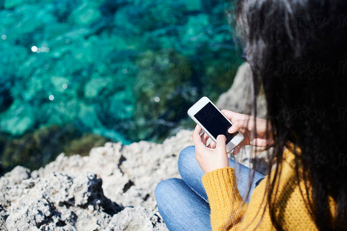Female texting on a smartphone next to the sea