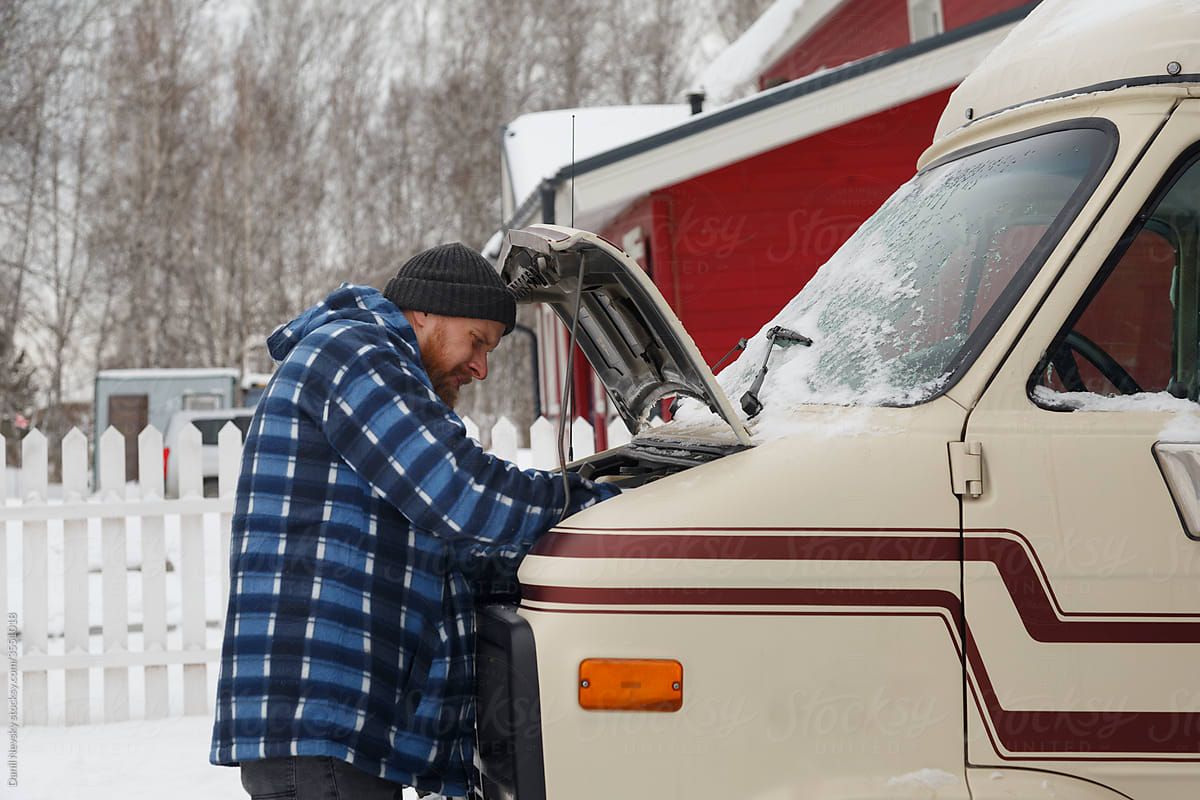 Bearded male repairing vehicle on cold winter day