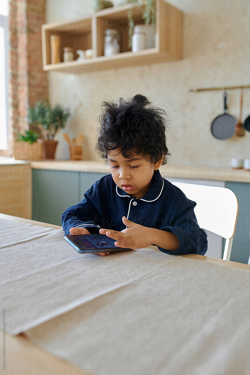 little boy of preschool age is sitting at a table with a phone