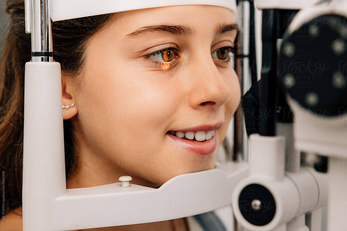 Cheerful girl sitting and looking into eye test machine