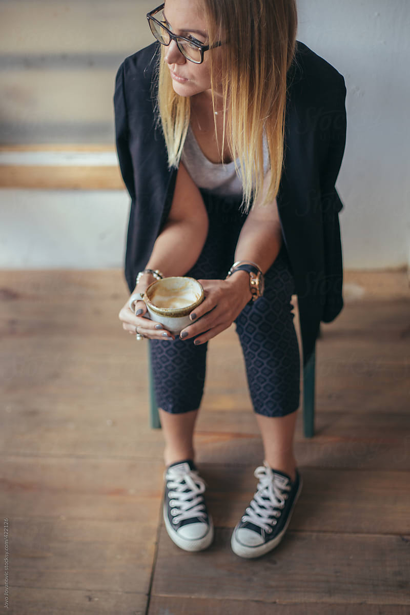 Blonde woman sitting and holding cup of coffee in her hands