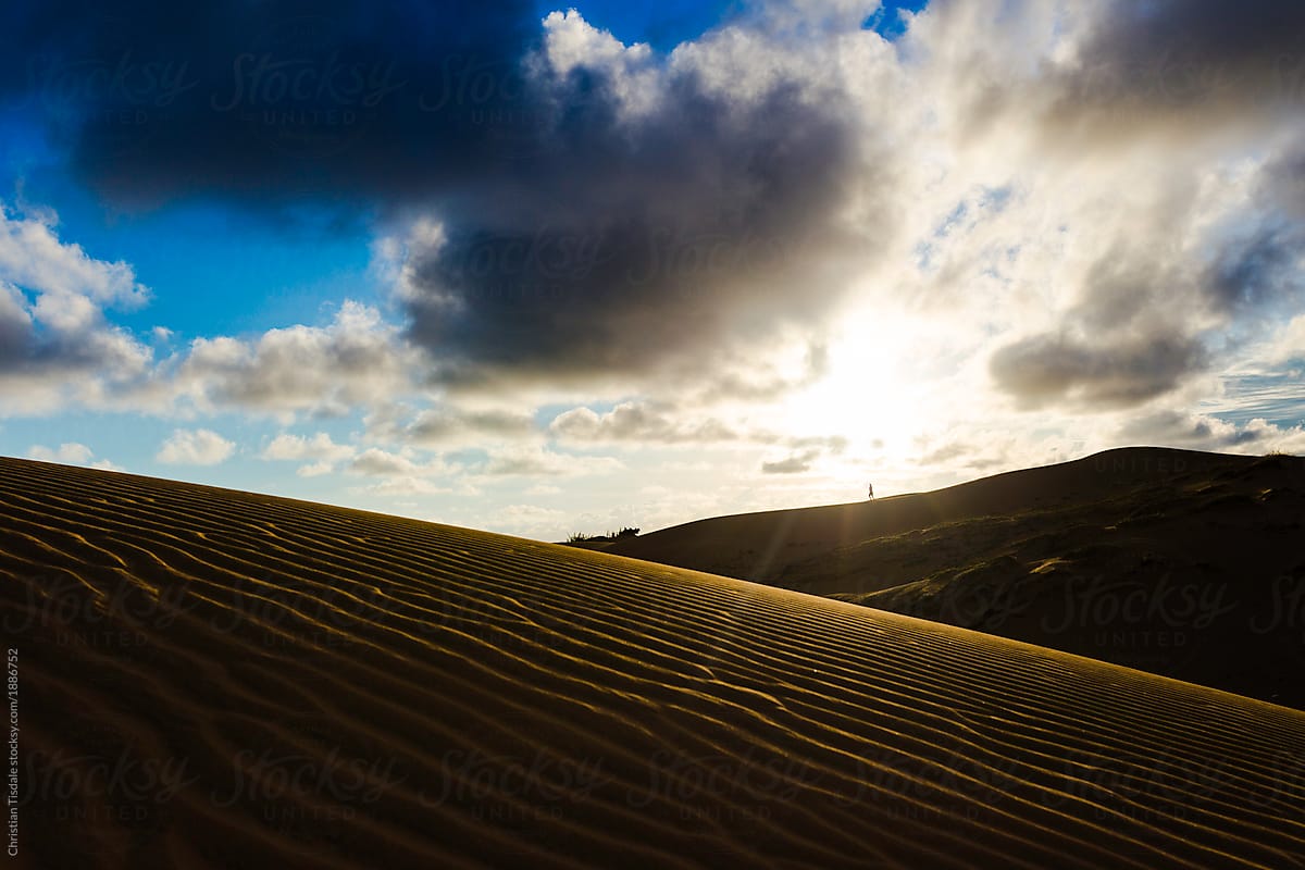 A distant figure walking across a sand dune at sunset