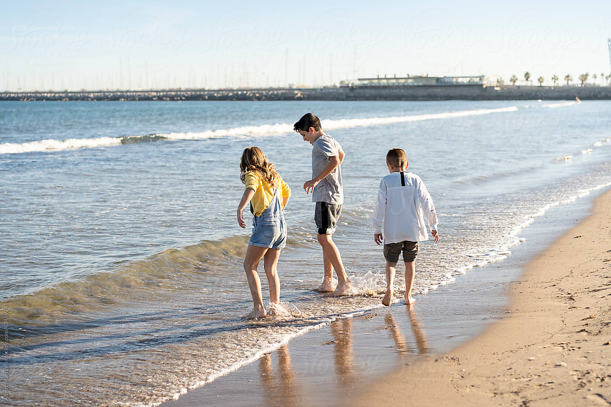 Cute siblings standing in water on sandy seashore