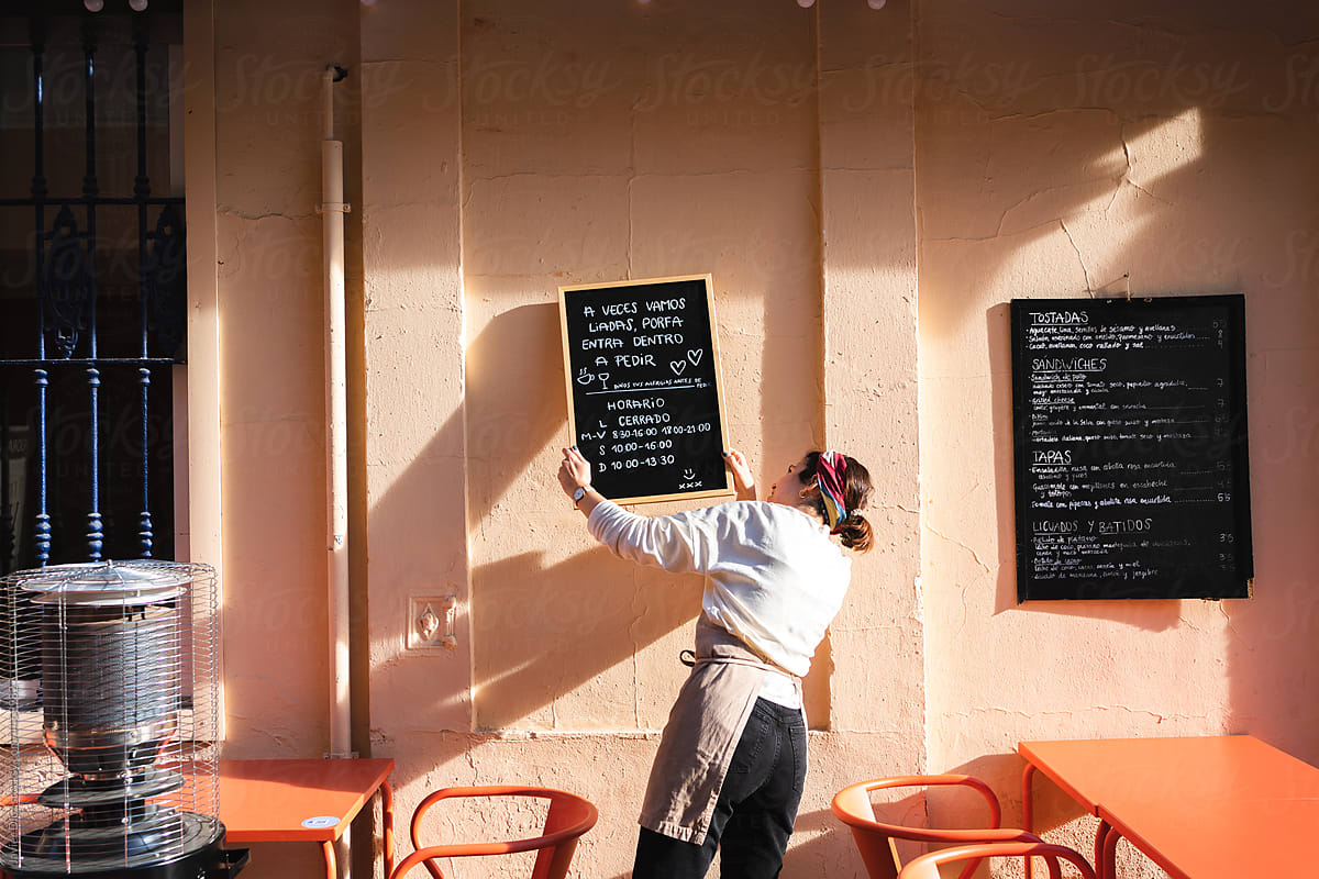 Waitress hanging whiteboards in street cafe