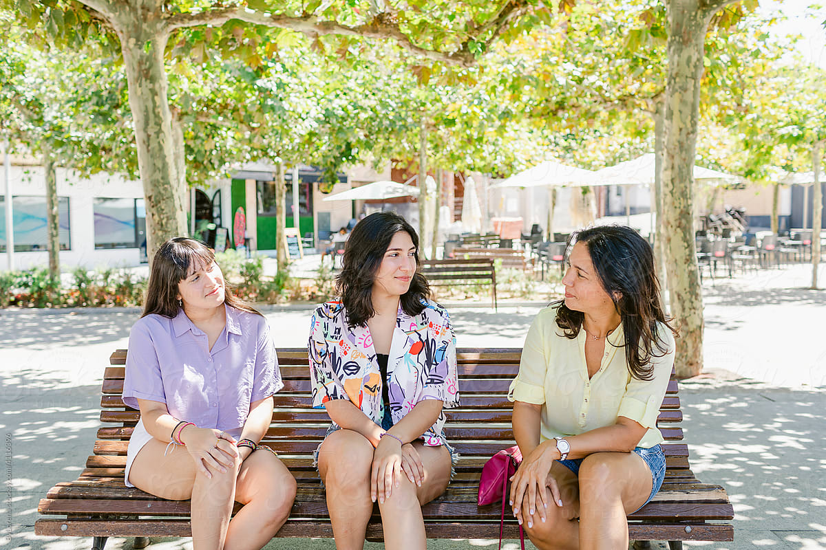Mother and teen daughters sitting on bench outdoors