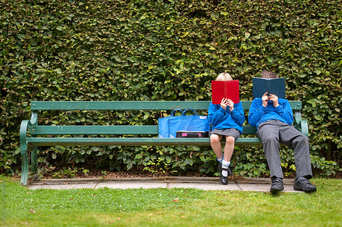 two children in school uniform reading books on a park bench