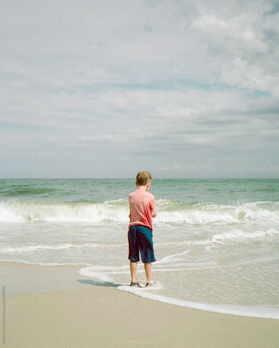 Boy standing on the beach looking trepidatiously at the water