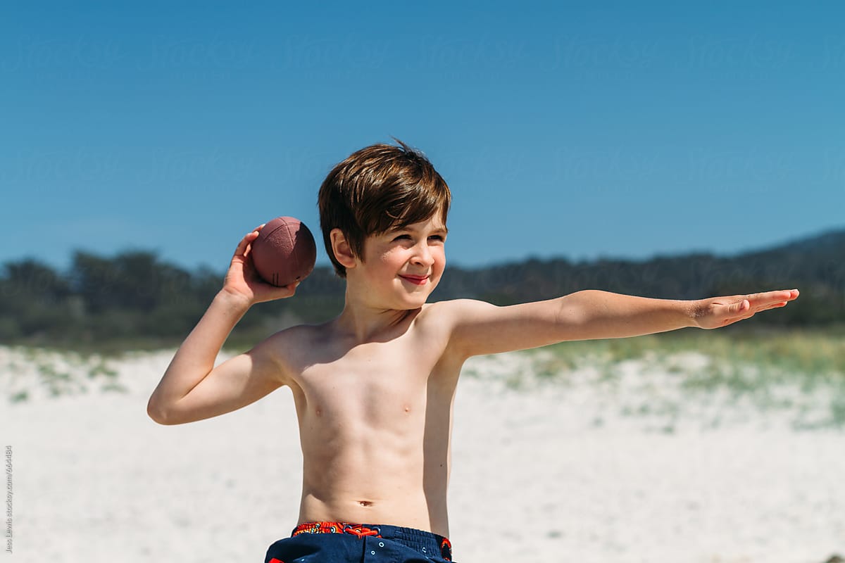 cute boy posing with toy football at the beach.