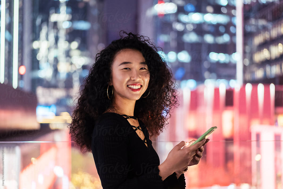 Woman playing phone in front of the night cityscape