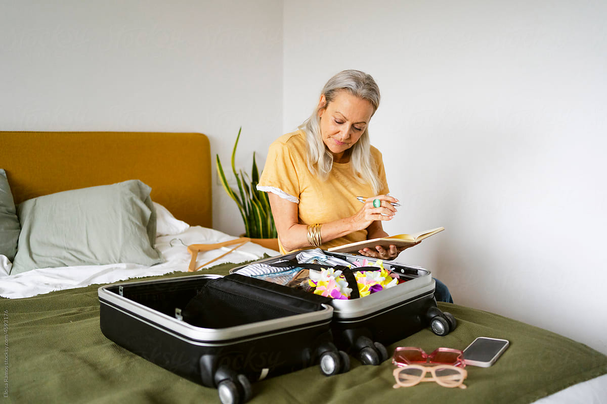 retired woman checking list on notebook by suitcase