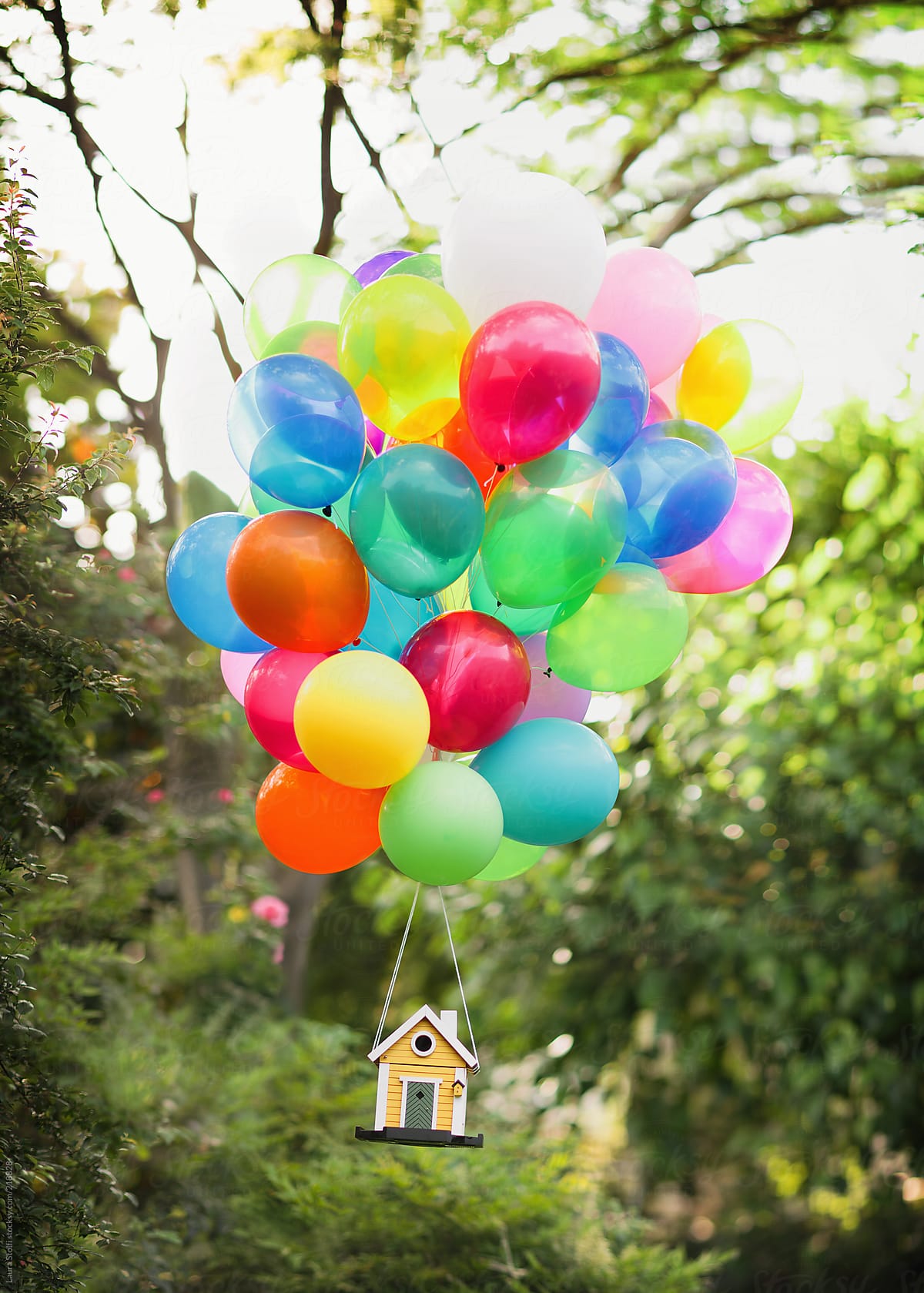 Yellow wooden house flying while lifted by bunch of colourful balloons