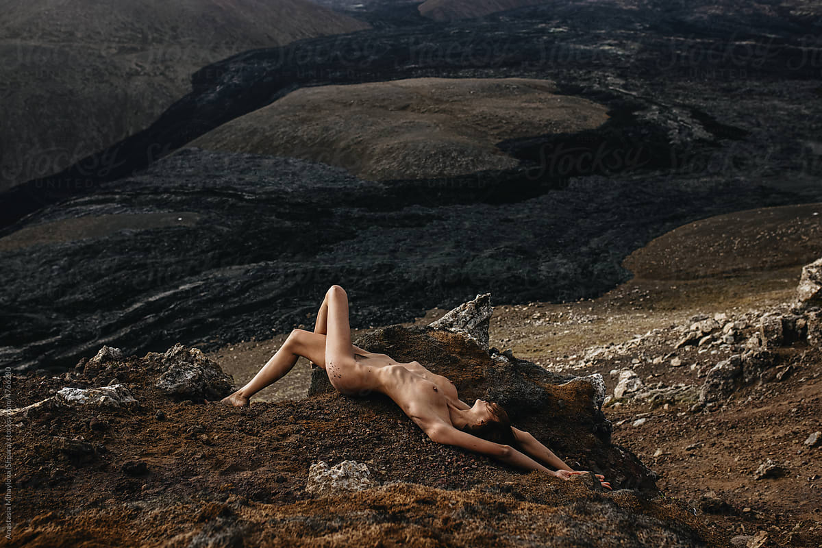 Naked woman lying in front of black lava river in Iceland