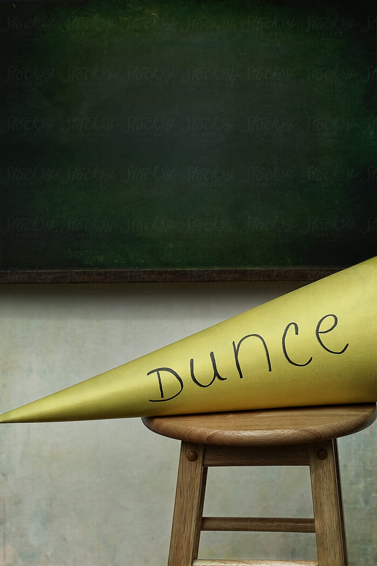 Closeup dunce hat on stool with chalkboard in background