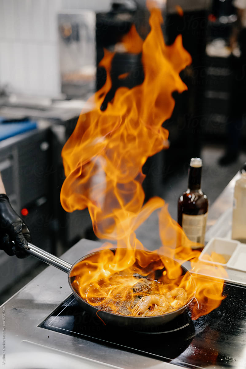Anonymous chef preparing prawns in burning frying pan