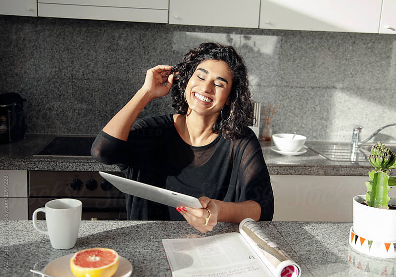 Woman laughing in a kitchen holding a tablet PC.