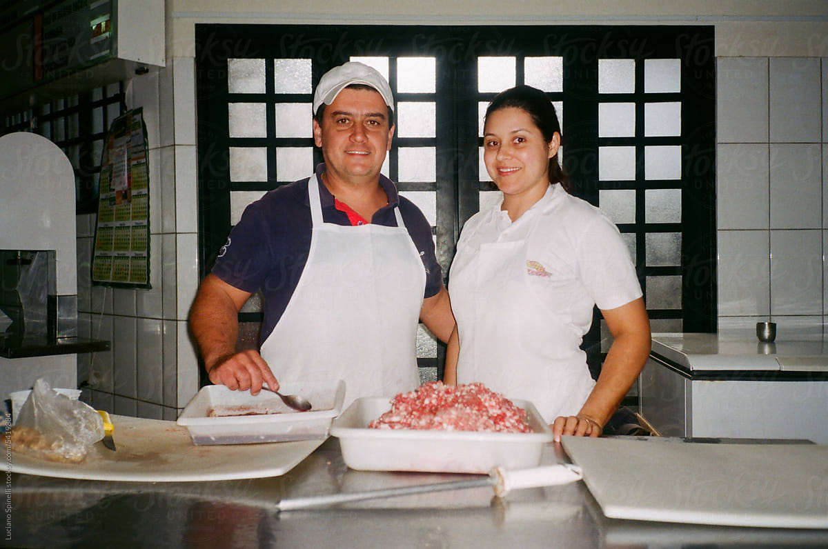 Man and woman stand in their butcher shop and tray with ground meat