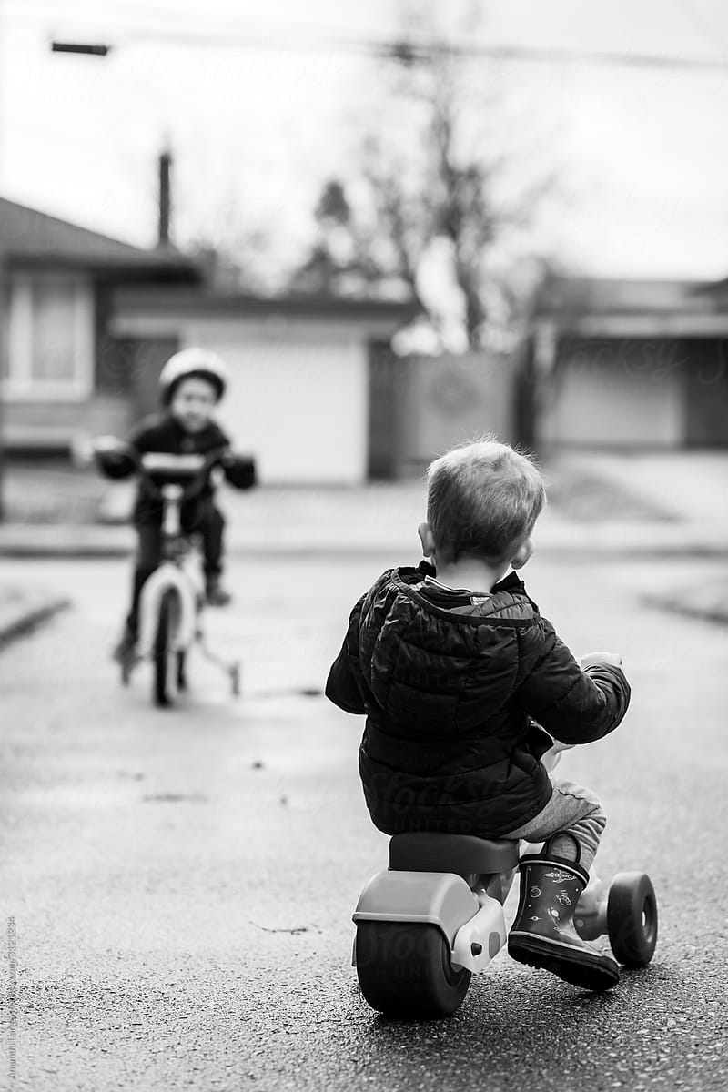 two young boys riding bikes on a suburban driveway