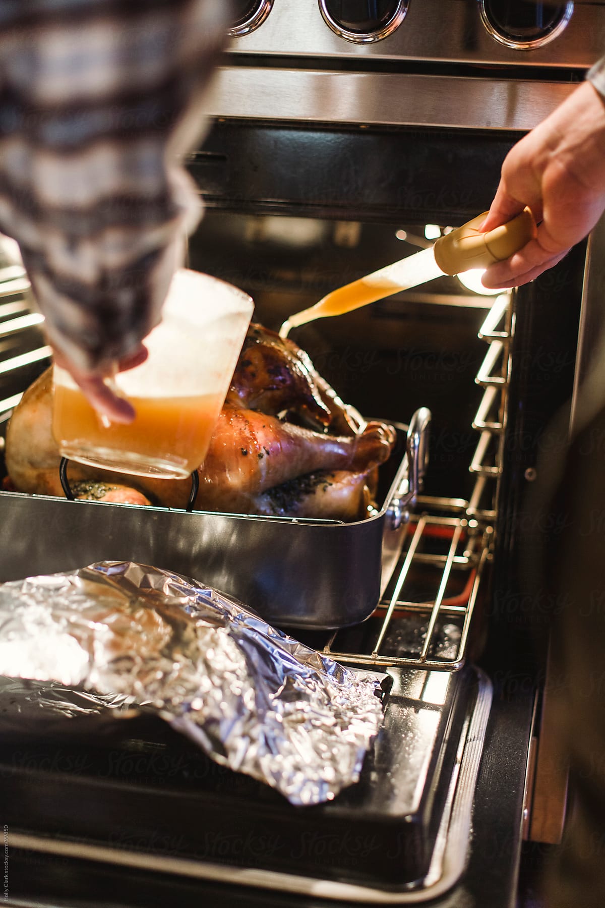 Man\'s arms basting turkey in oven on Thanksgiving day