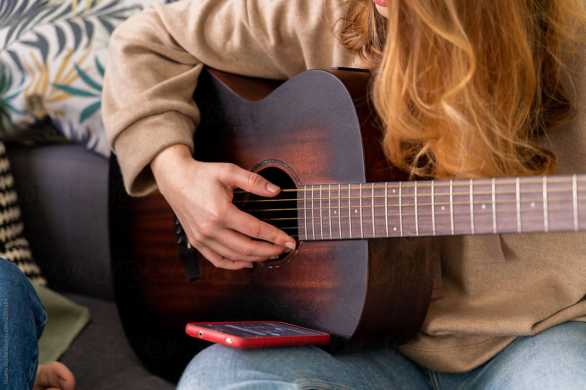 Woman tuning guitar with phone