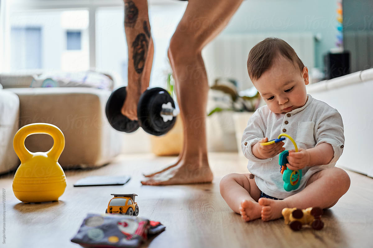 Anonymous father doing workout at home while his baby is playing at the living room