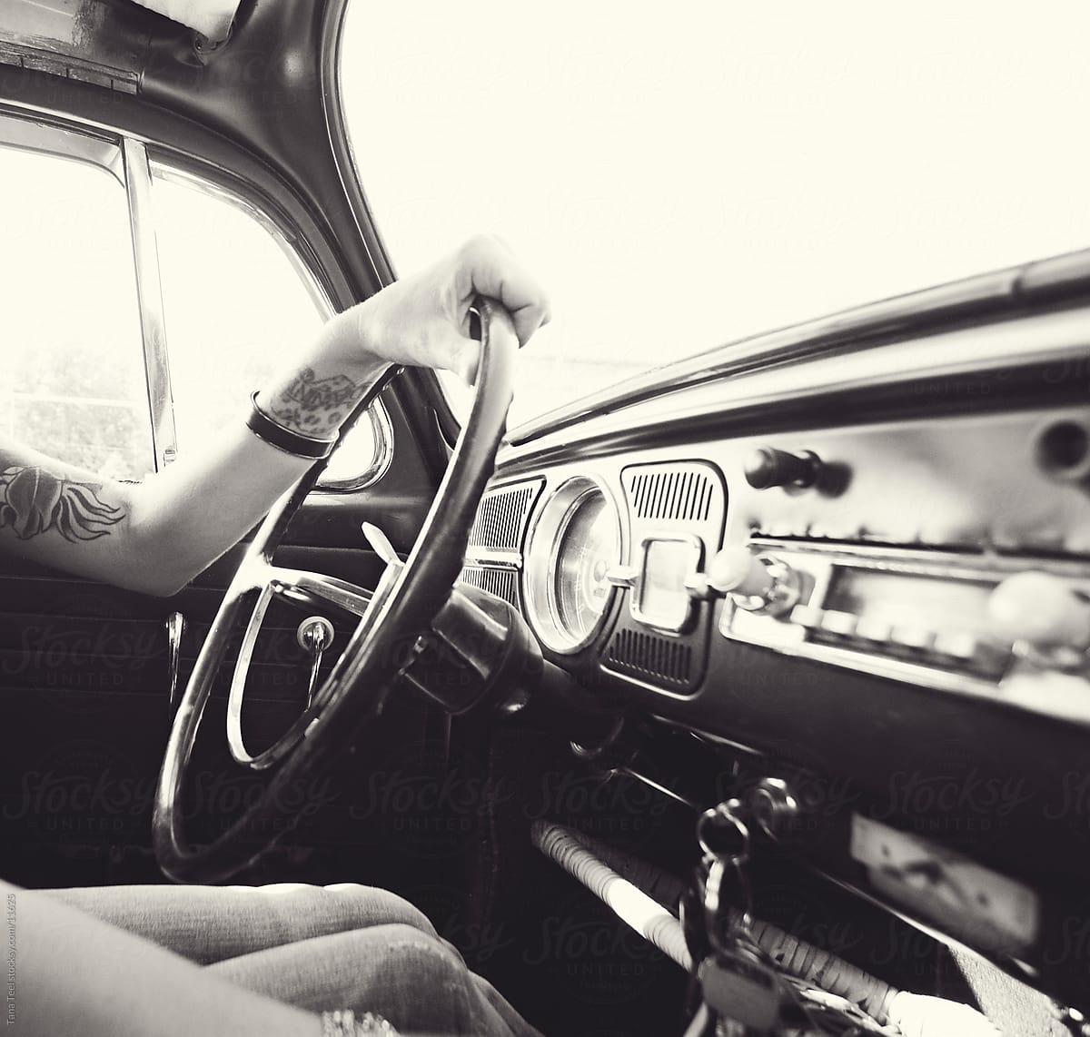 Woman sitting behind steering wheel of vintage car.