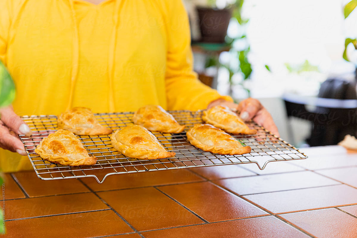 Woman in a yellow shirt holding a rack of Argentinian empanadas
