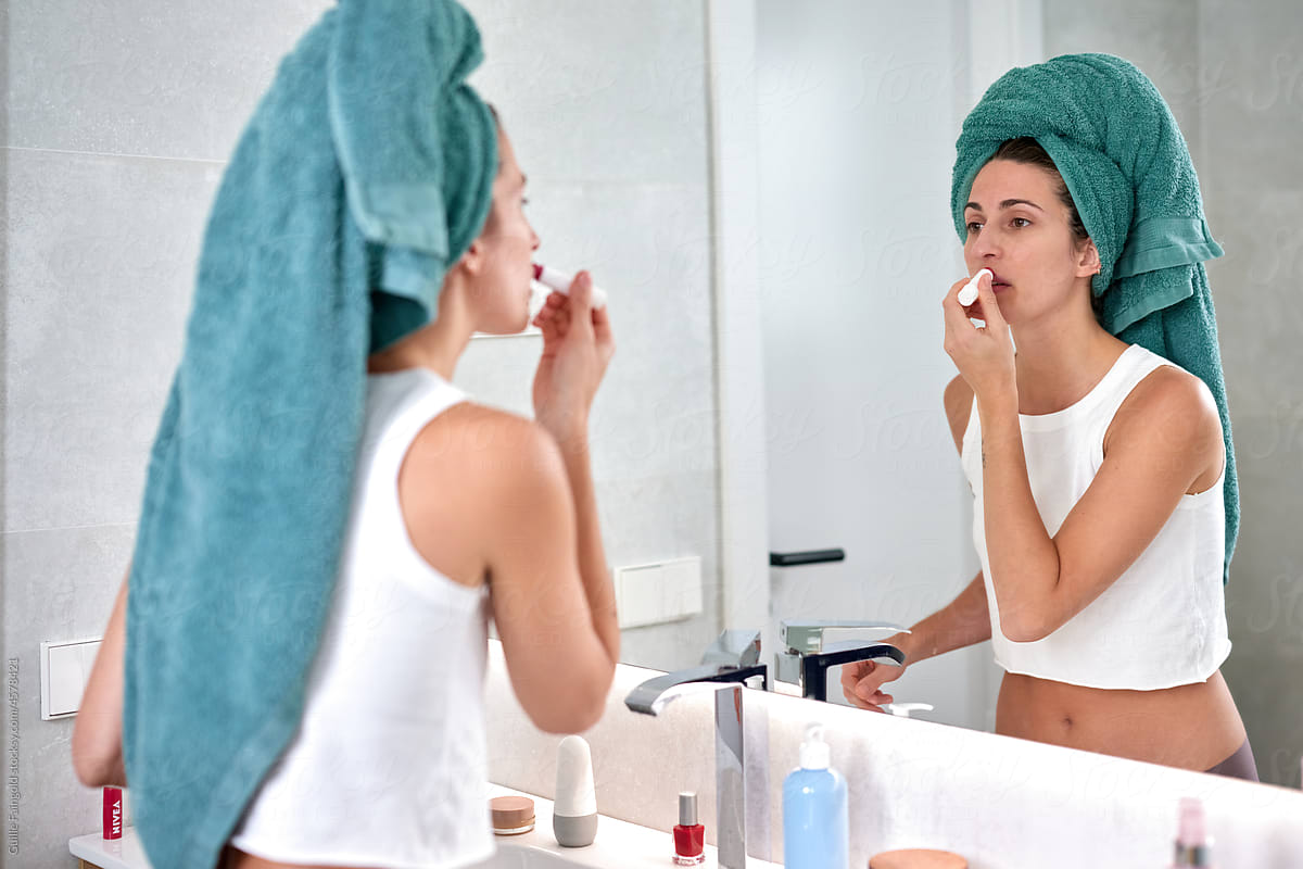Reflexed Woman in mirror applying balm in morning