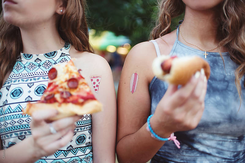 Two young friends eating pizza and hot dogs at a carnival