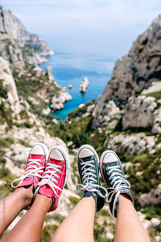 Two friends hanging their feet down towards cliffs / ocean coast