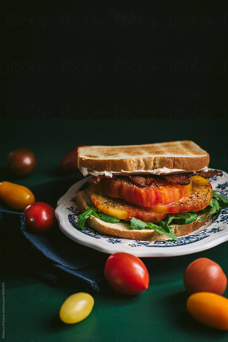Heirloom tomato sandwich with bacon surrounded by cherry tomatoes