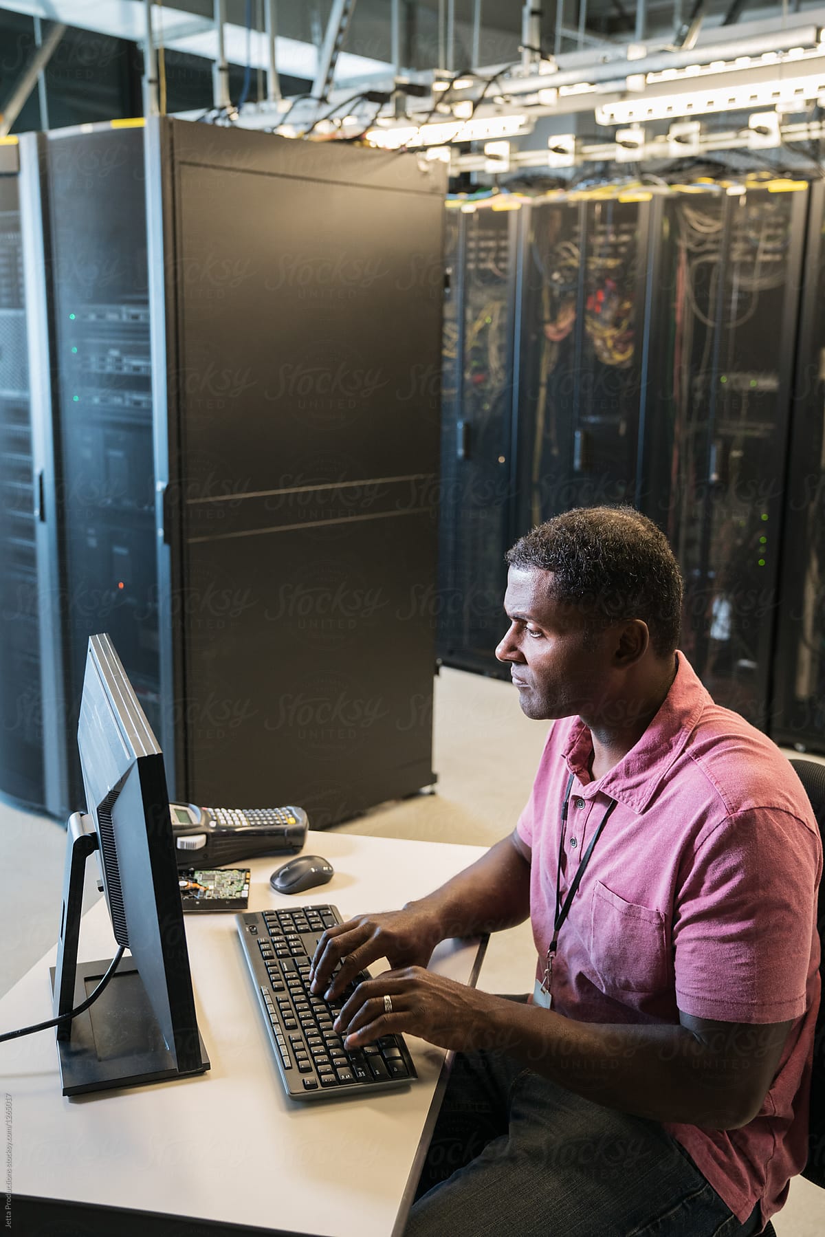 Black male technician works at a computer in a server room