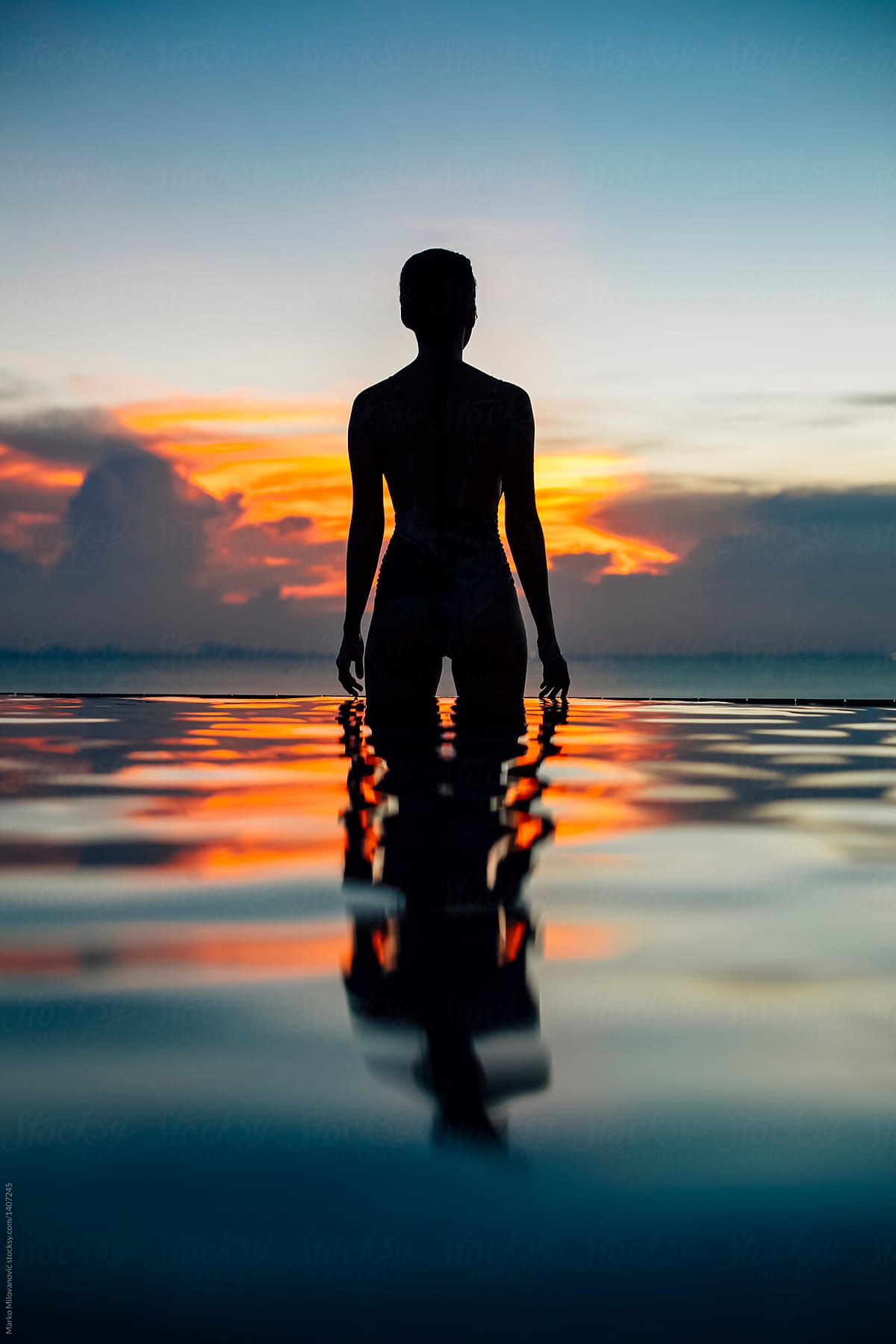 Silhouette of a woman in pool above the sea with water reflection