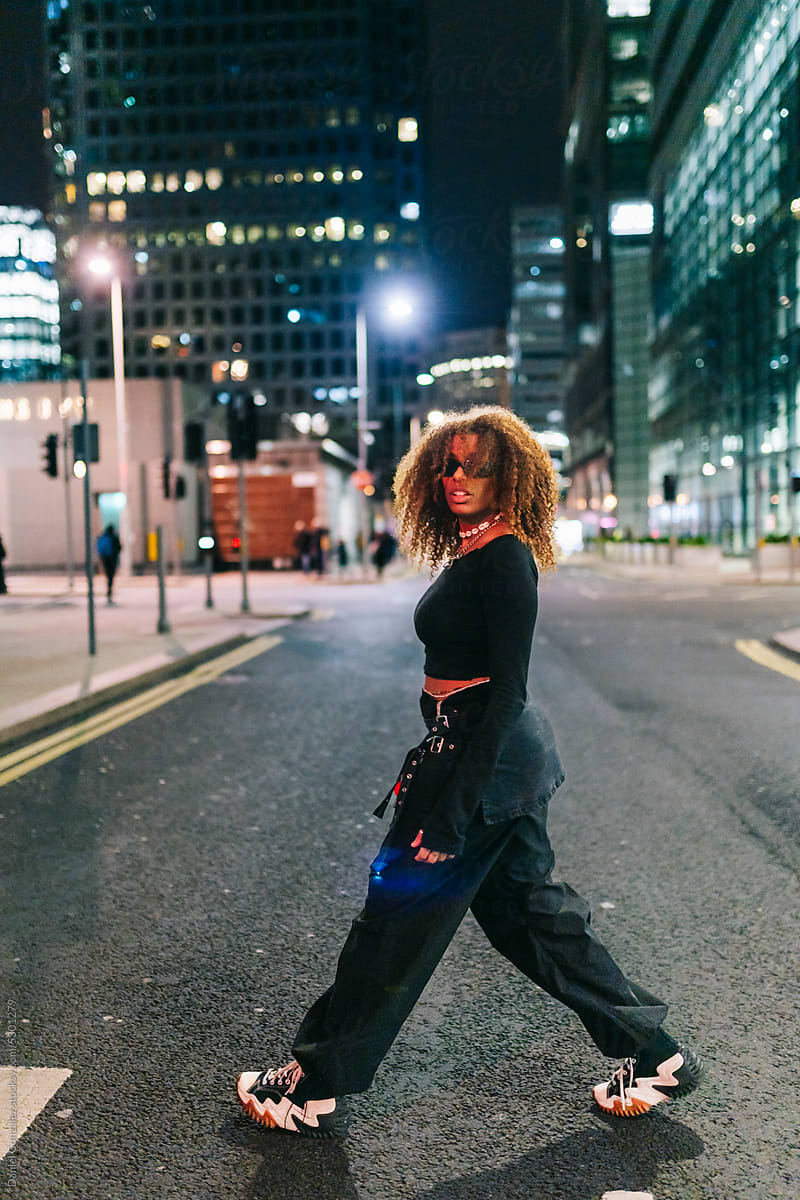 Stylish Black woman walking on street at night