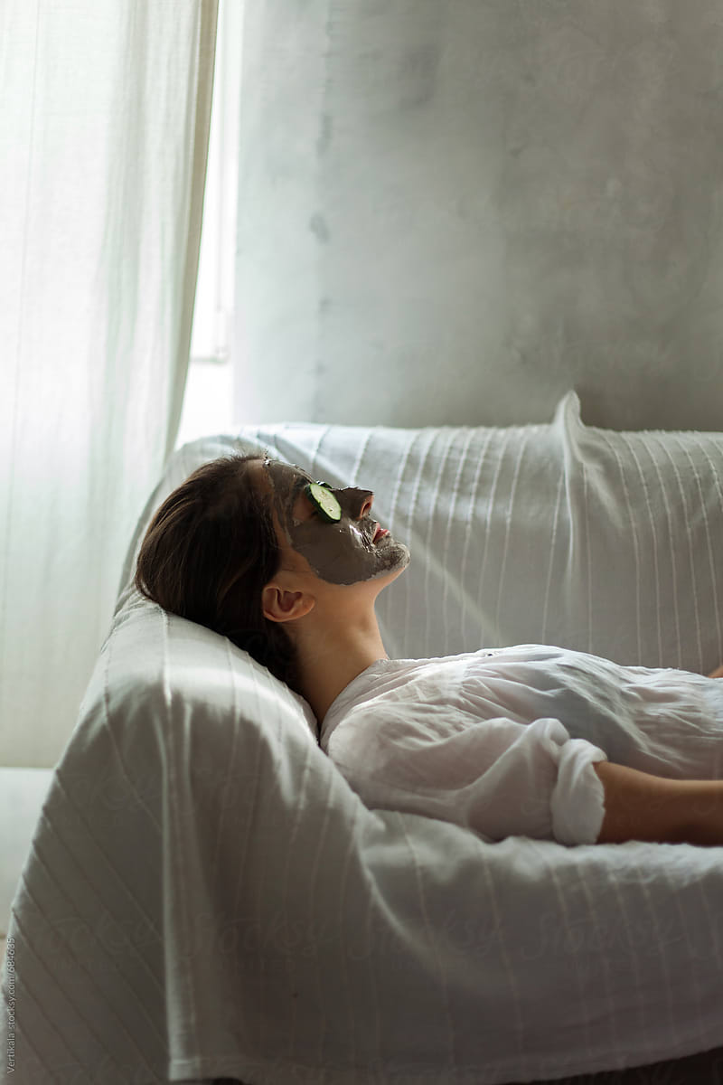 Woman lying on a couch with mask and cucumbers on her face