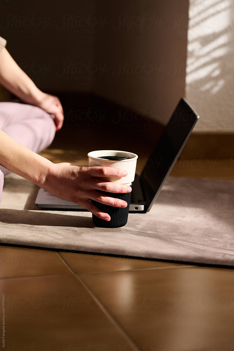 Yogi Holding Reusable Coffee Cup by Laptop on Floor