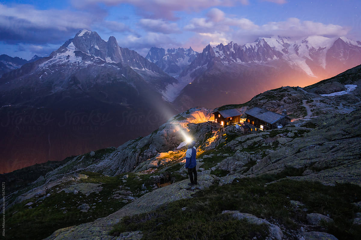 Man with headlamp near mountain refuge at twilight