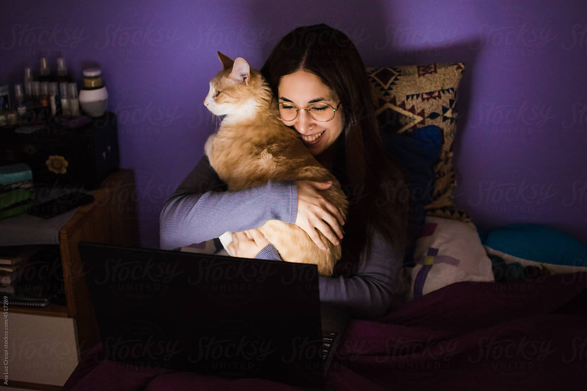 Happy woman watching a movie with her cat in bed
