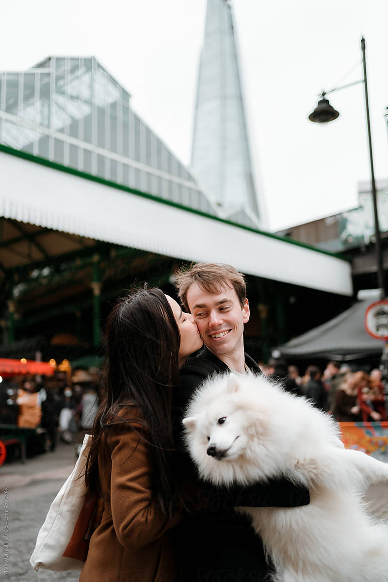 A couple holds their dog and has a romantic moment in the city