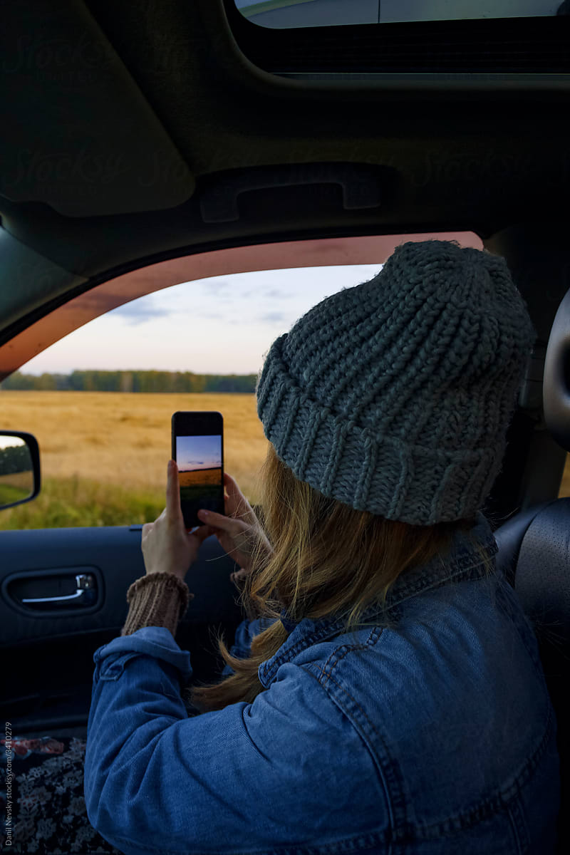 Female traveler taking photos of countryside from car