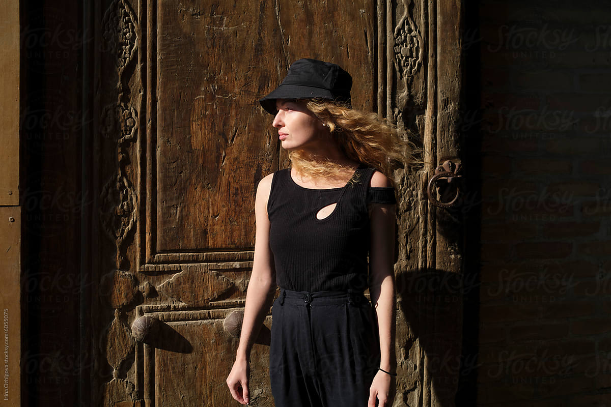 Elegant Woman in Black Dress and Hat Standing by an Ornate Wooden Door