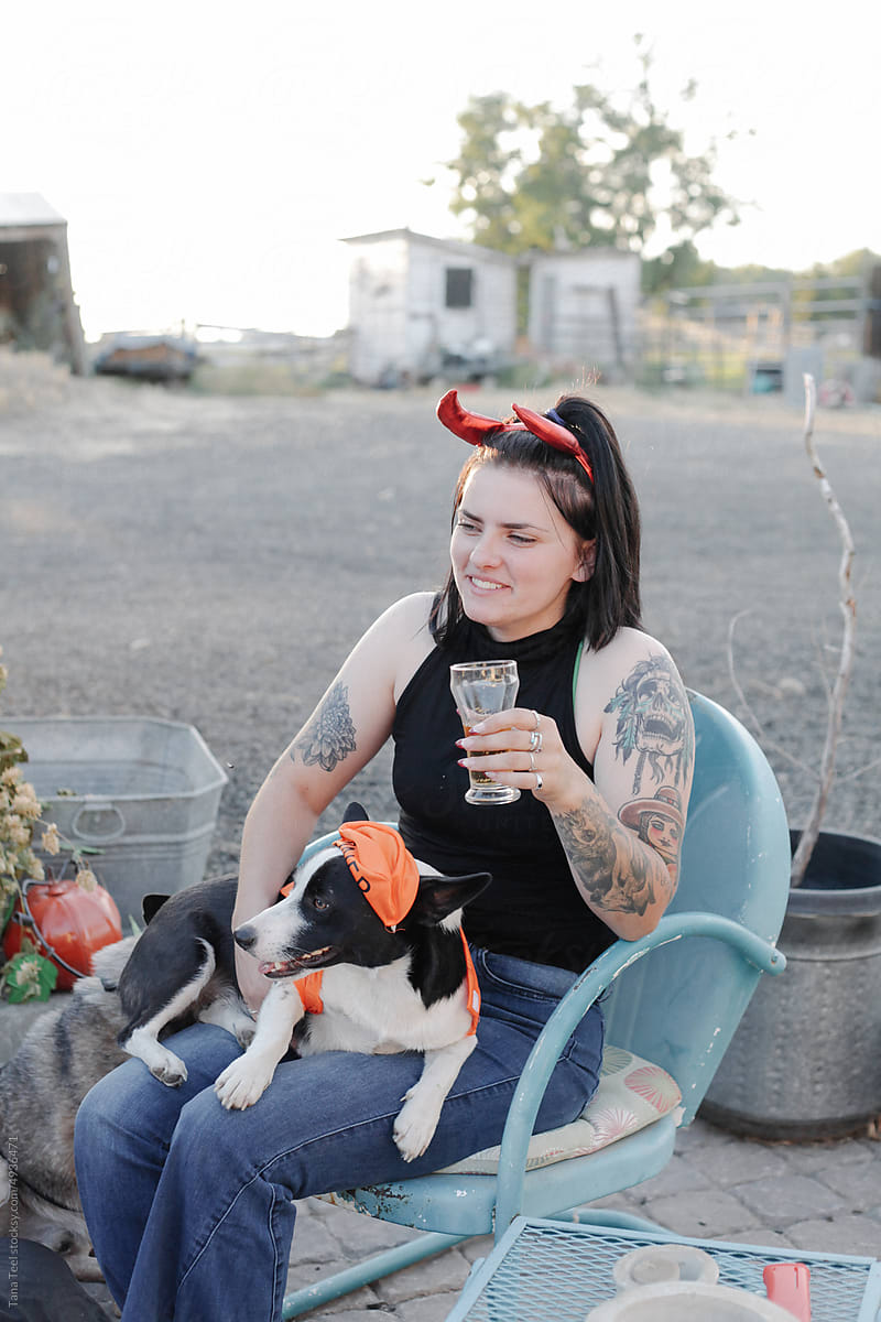woman in partial costume relaxes with dog in costume on patio